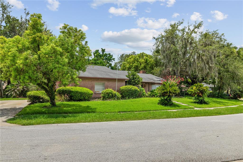 A single-story brick house sits behind a green lawn with mature trees and shrubs — 115 KAYWOOD DRIVE, SANFORD, FL