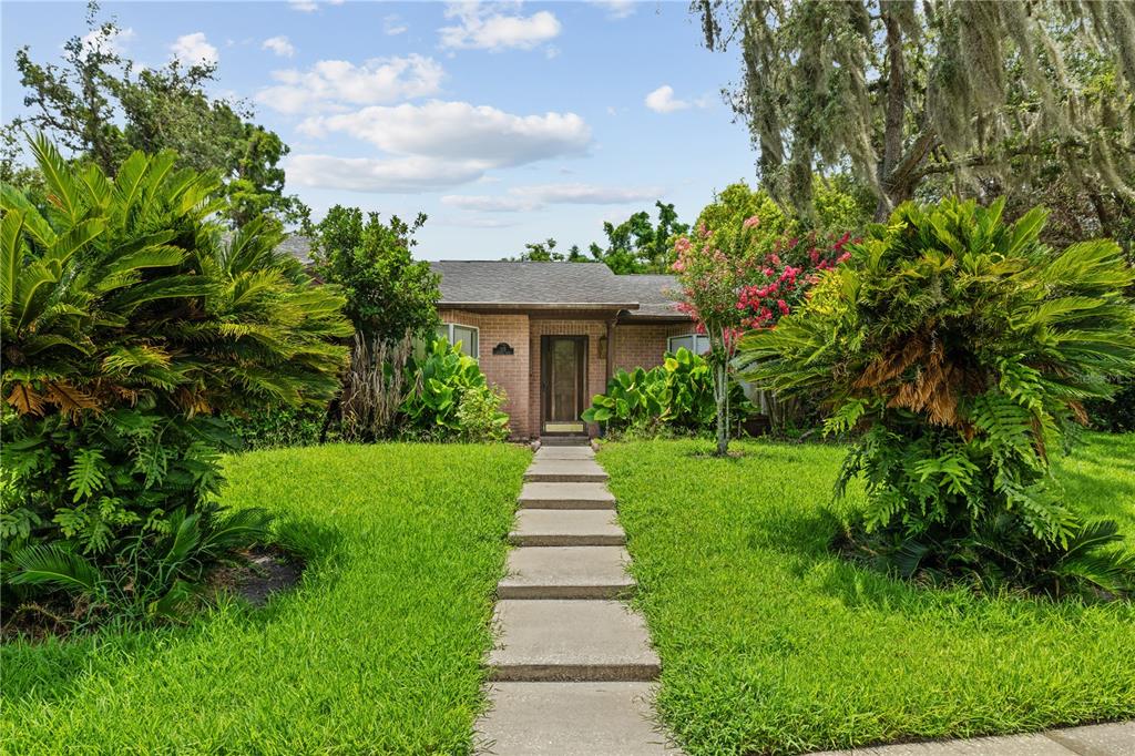 A brick house with a concrete walkway leading to the front door, flanked by palm-like plants — 115 KAYWOOD DRIVE, SANFORD, FL