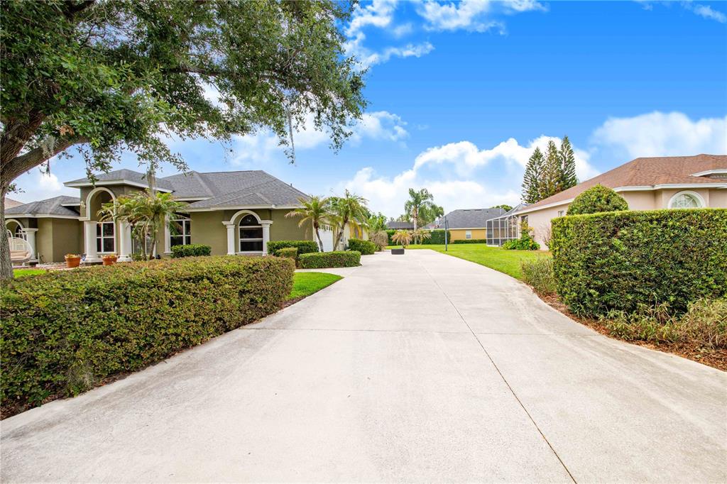 A long concrete driveway leads toward a house with a large tree and hedges — 445 TALAMONE DRIVE, WINTER HAVEN, FL