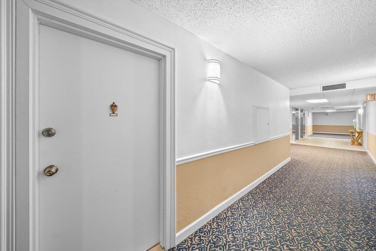 A white door with a peephole opens into a carpeted hallway with beige wainscoting — 3460 S Ocean Boulevard # 6150, Palm Beach FL 33480, PALM BEACH, FL
