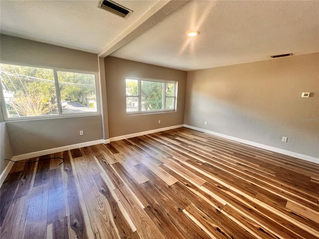 An empty room features wood-look flooring, beige walls, and two large windows — 1110 POINSETTIA AVENUE UNIT B, ORLANDO, FL