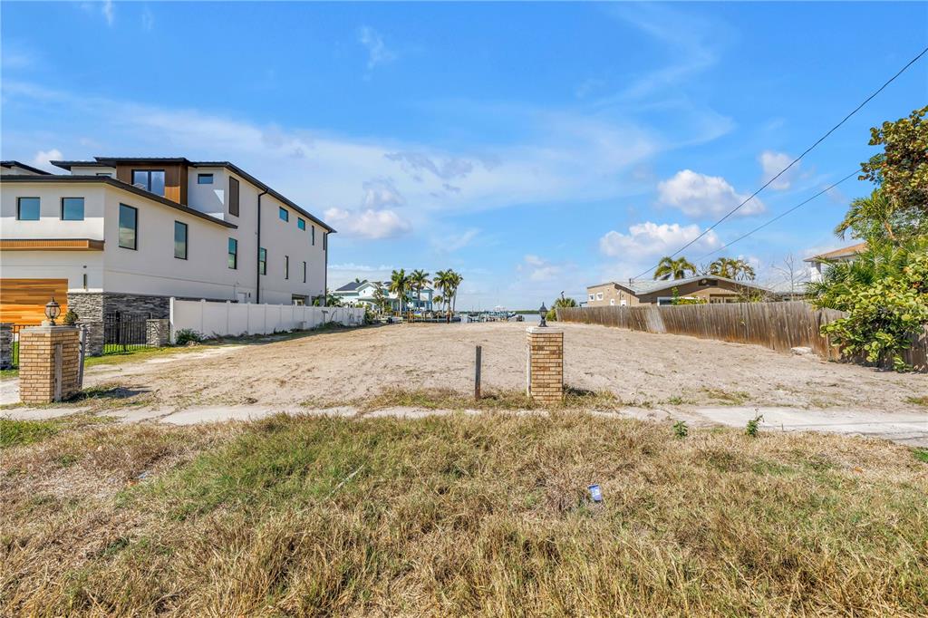 A vacant, sandy residential lot sits between a modern multi-story house and a wooden fence — 2129 BAYOU GRANDE BOULEVARD NE, ST PETERSBURG, FL