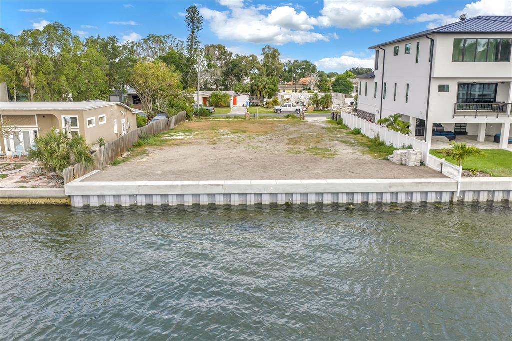 An aerial view shows a vacant waterfront lot with a concrete seawall between two houses — 2129 BAYOU GRANDE BOULEVARD NE, ST PETERSBURG, FL