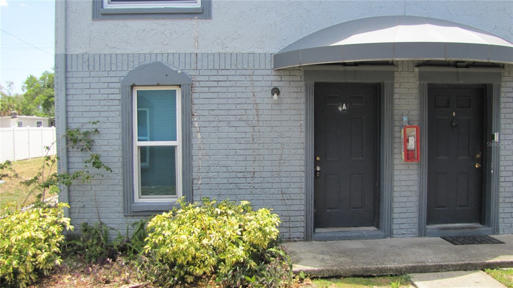 The exterior of a gray brick building features two black doors and a metal awning — 5116 TEMPLE HEIGHTS ROAD UNIT A, TAMPA, FL