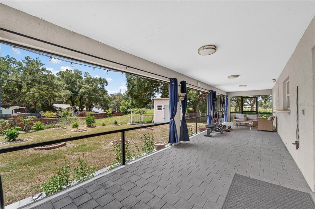 A covered patio features gray paver flooring, a screened-in wall, and a view of the backyard — 1459 WYNGATE LANE, LAKELAND, FL