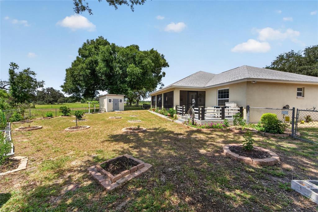 A backyard with a house, a small shed, and several circular brick-lined garden beds — 1459 WYNGATE LANE, LAKELAND, FL