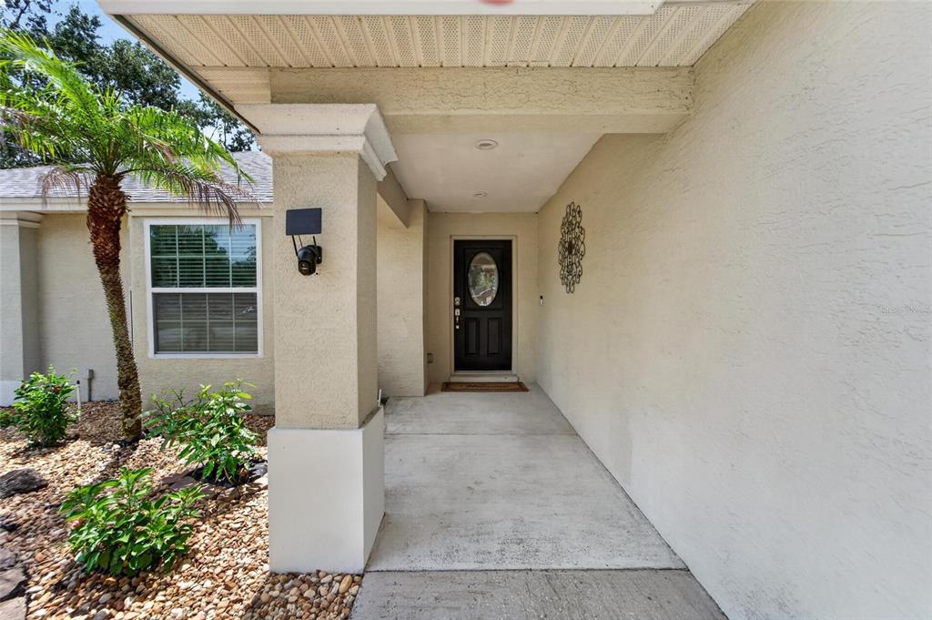 A covered concrete porch leads to a dark front door with an oval glass insert — 1459 WYNGATE LANE, LAKELAND, FL