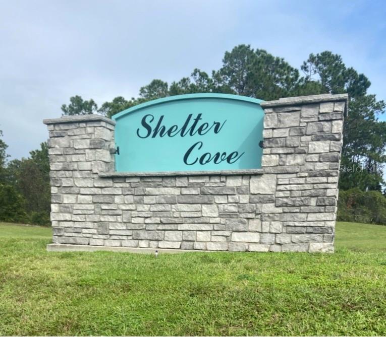 A stone monument sign with a teal arched panel reads Shelter Cove in a grassy area — 1310 PINE ISLAND DRIVE N, ST CLOUD, FL