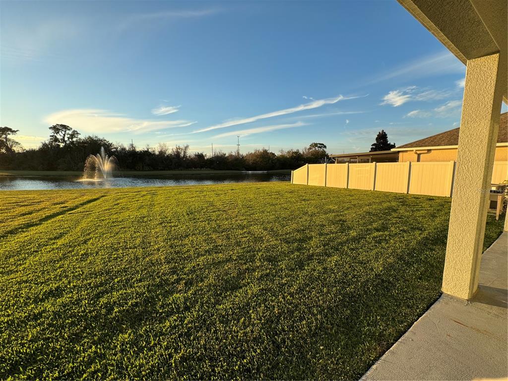 A backyard view featuring a grassy lawn, a pond with a fountain, and a fence — 11523 PERU SPRINGS PLACE, RIVERVIEW, FL