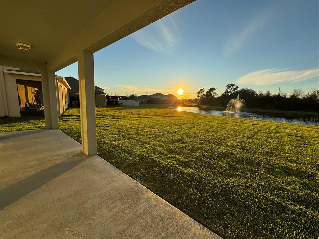 A covered patio overlooks a grassy backyard with a pond and a water fountain at sunset — 11523 PERU SPRINGS PLACE, RIVERVIEW, FL