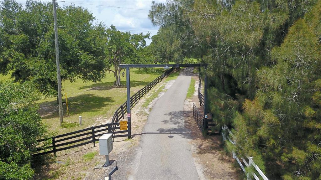 An aerial view shows a paved driveway leading through a gated entrance into a field — 16945 W PHIL C PETERS ROAD, WINTER GARDEN, FL