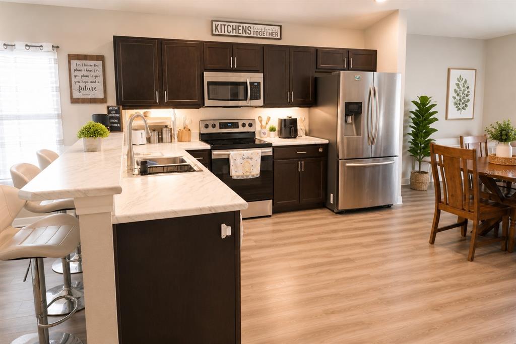 A kitchen features dark wood cabinets, white marble-look countertops, stainless steel appliances, and bar seating — 8016 DIAMOND CREEK LANE, LAKELAND, FL