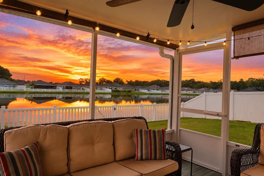 A screened-in patio with wicker furniture overlooks a lake at sunset — 8016 DIAMOND CREEK LANE, LAKELAND, FL