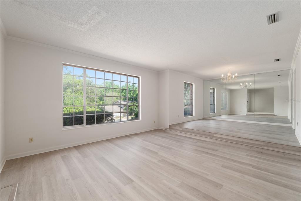 A living room with light wood-look flooring, a sunken area, and a large mirrored wall — 1410 NW 28TH STREET, GAINESVILLE, FL