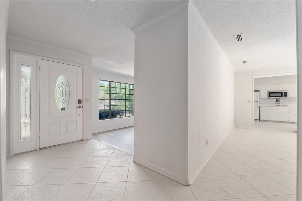 A white-walled entryway with tile flooring leads to a living area and a kitchen — 1410 NW 28TH STREET, GAINESVILLE, FL