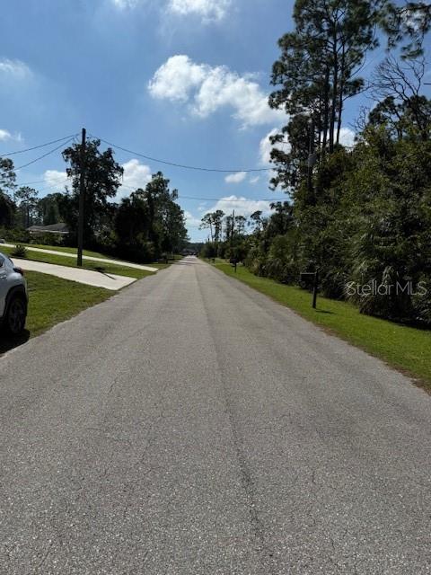 A paved residential street stretches into the distance under a blue sky with scattered clouds — PINCUSHION STREET, NORTH PORT, FL