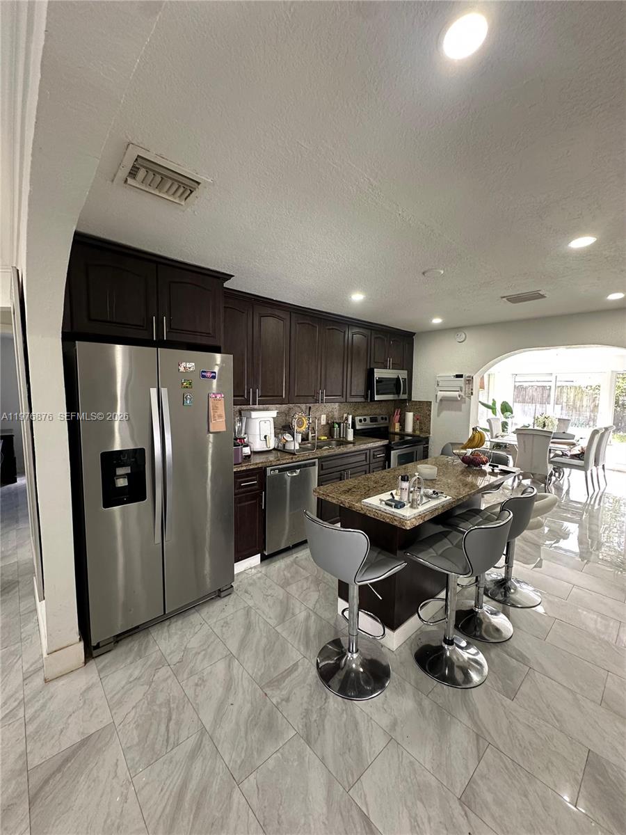 A kitchen features dark wood cabinets, stainless steel appliances, a granite island, and tiled floors — 5710 Douglas St, Hollywood FL 33021, HOLLYWOOD, FL