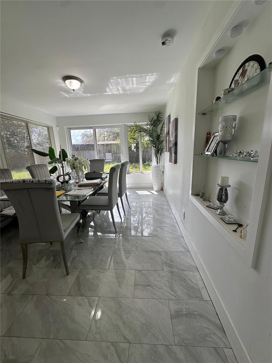 A dining room features gray tile flooring, a glass-top table, and a built-in wall niche — 5710 Douglas St, Hollywood FL 33021, HOLLYWOOD, FL