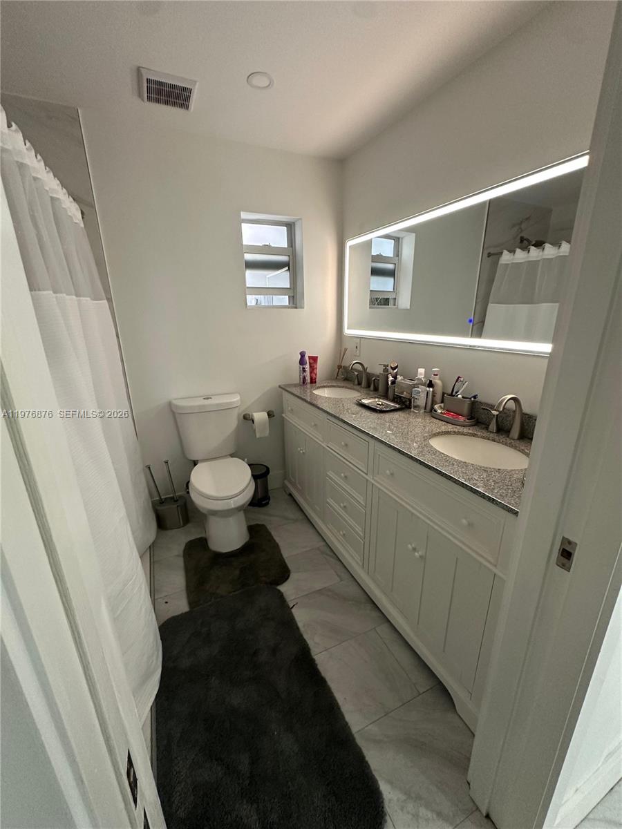 This bathroom features a double vanity with a granite countertop and a walk-in shower — 5710 Douglas St, Hollywood FL 33021, HOLLYWOOD, FL