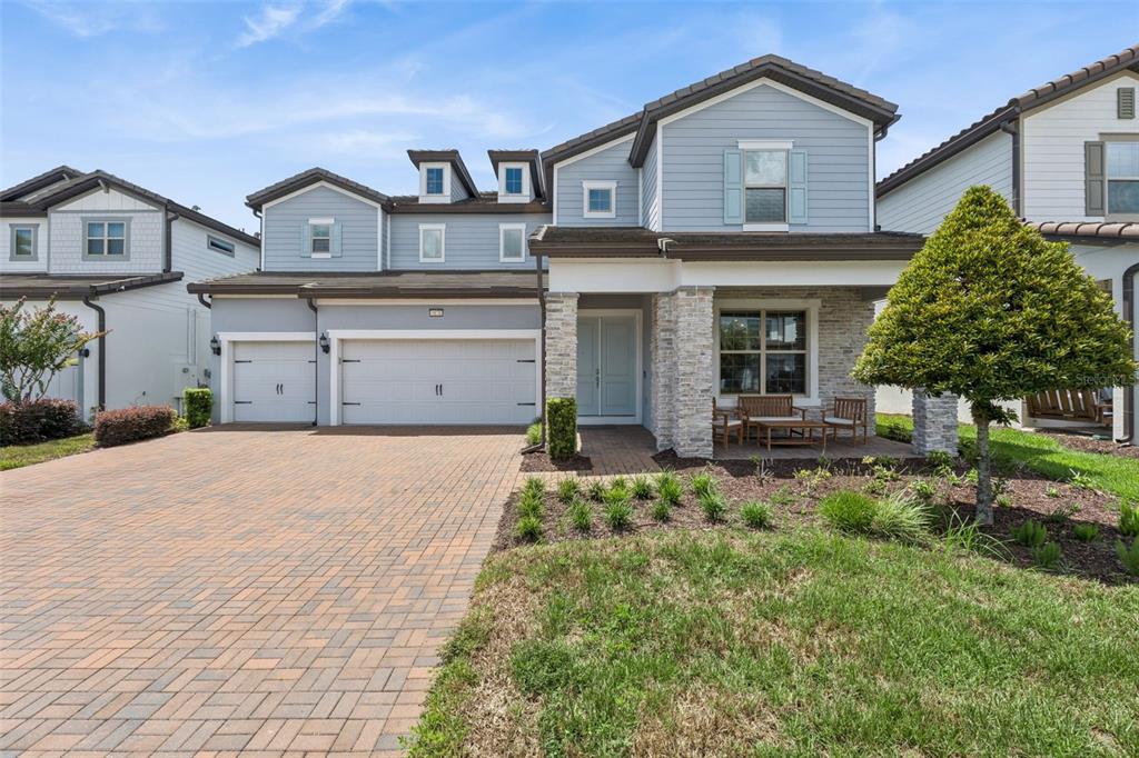A two-story suburban house with a brick paver driveway, three-car garage, and stone-accented front porch — 9070 WOODLAND FOREST ROAD, ORLANDO, FL