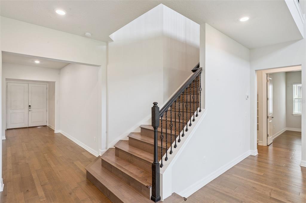 A foyer features hardwood floors, a staircase with dark wood railings, and white walls — 9070 WOODLAND FOREST ROAD, ORLANDO, FL