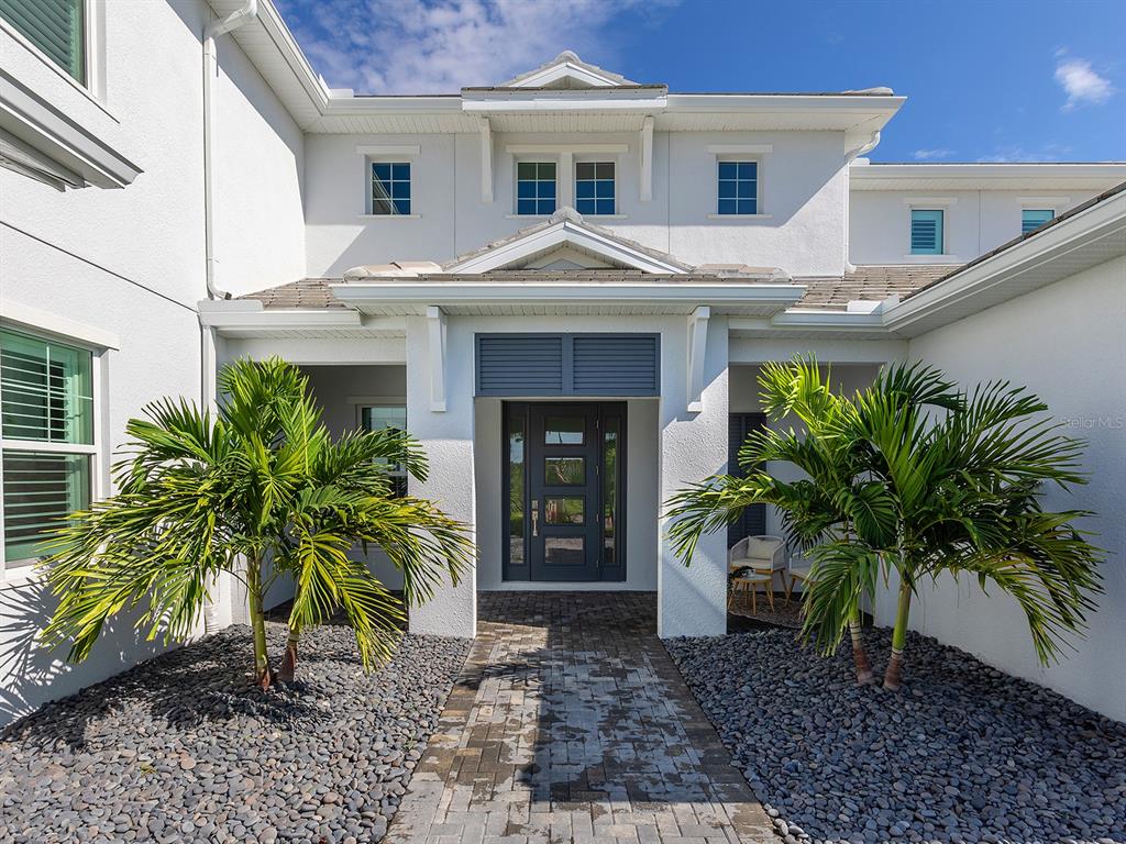 The exterior of a white house features a paved walkway, two palm trees, and a front door — 17974 PALMISTE DRIVE, LAKEWOOD RANCH, FL