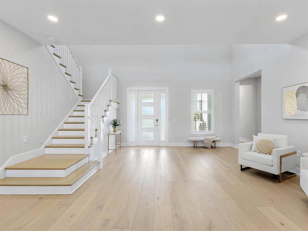 A bright entryway features light wood flooring, a white staircase, and a modern front door — 17974 PALMISTE DRIVE, LAKEWOOD RANCH, FL