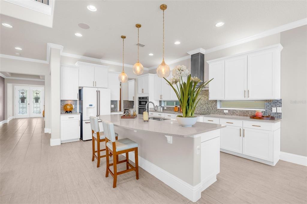 A modern kitchen features white cabinetry, a large quartz island, and three glass pendant lights — 9270 ROYAL ESTATES BOULEVARD, ORLANDO, FL