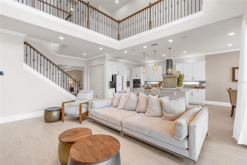 An open-concept living room and kitchen feature high ceilings, a staircase, and neutral furniture — 9270 ROYAL ESTATES BOULEVARD, ORLANDO, FL