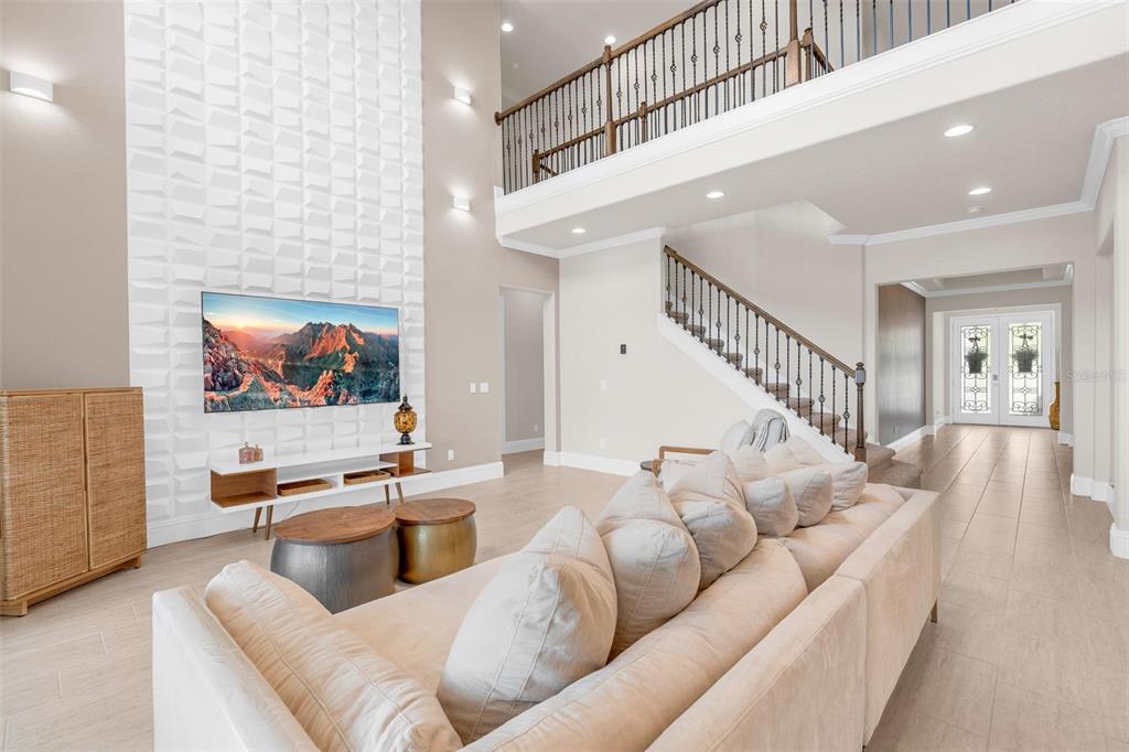A spacious living room features a textured white accent wall, a television, and a staircase — 9270 ROYAL ESTATES BOULEVARD, ORLANDO, FL