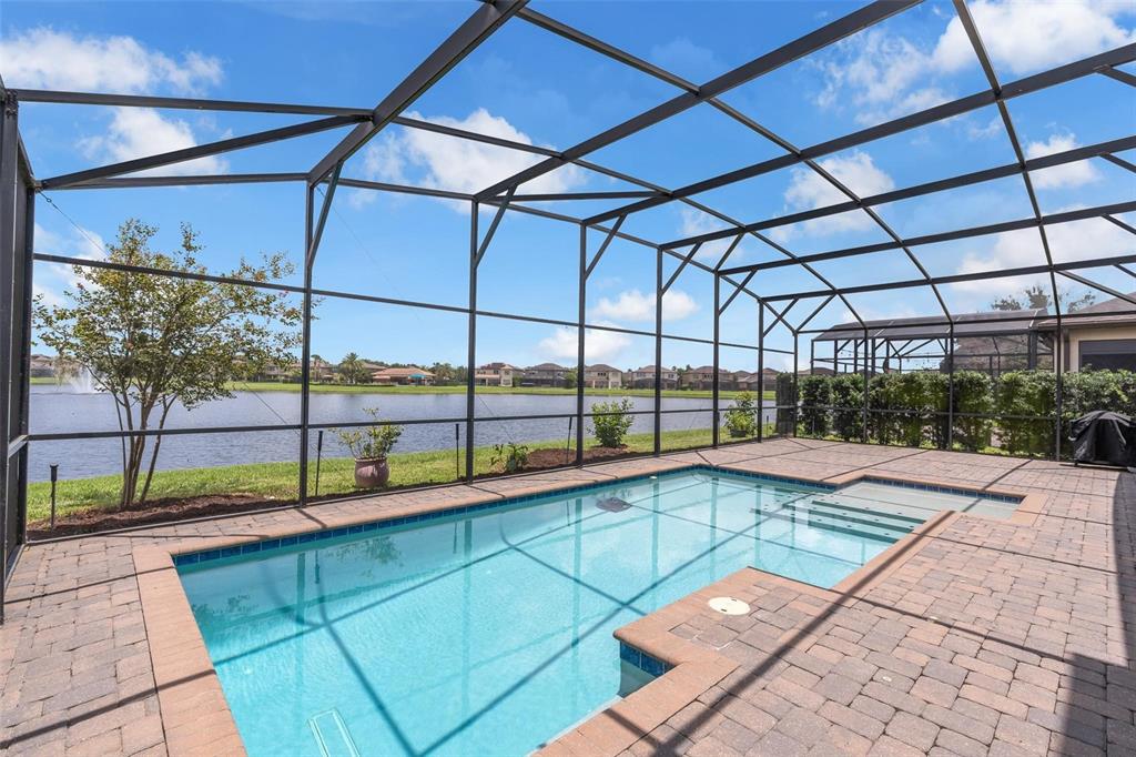 A screened-in pool patio overlooks a lake with a fountain under a blue sky — 9270 ROYAL ESTATES BOULEVARD, ORLANDO, FL