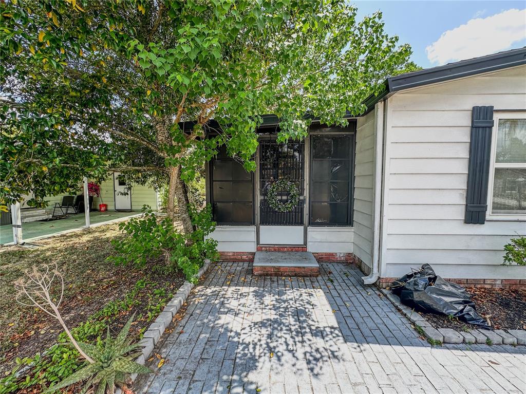 A paved walkway leads to the screened front entrance of a white house with shutters — 1820 W SCHWARTZ BOULEVARD, LADY LAKE, FL