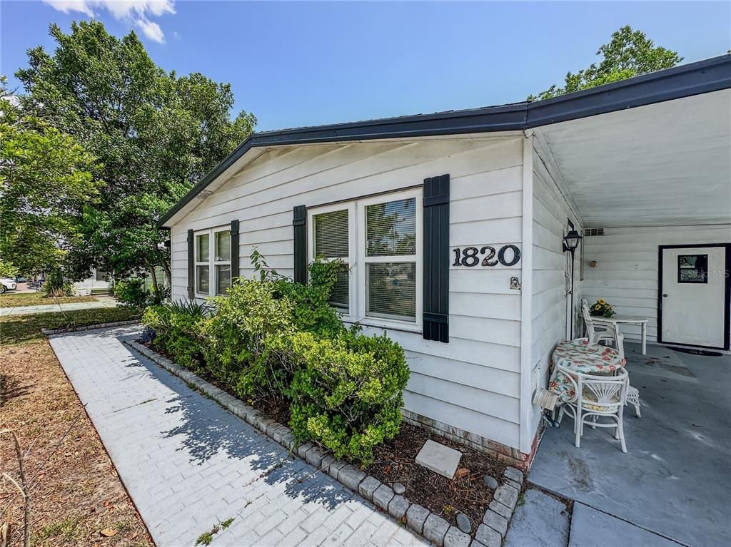 A white house exterior features a paved walkway, green bushes, and a covered patio area — 1820 W SCHWARTZ BOULEVARD, LADY LAKE, FL