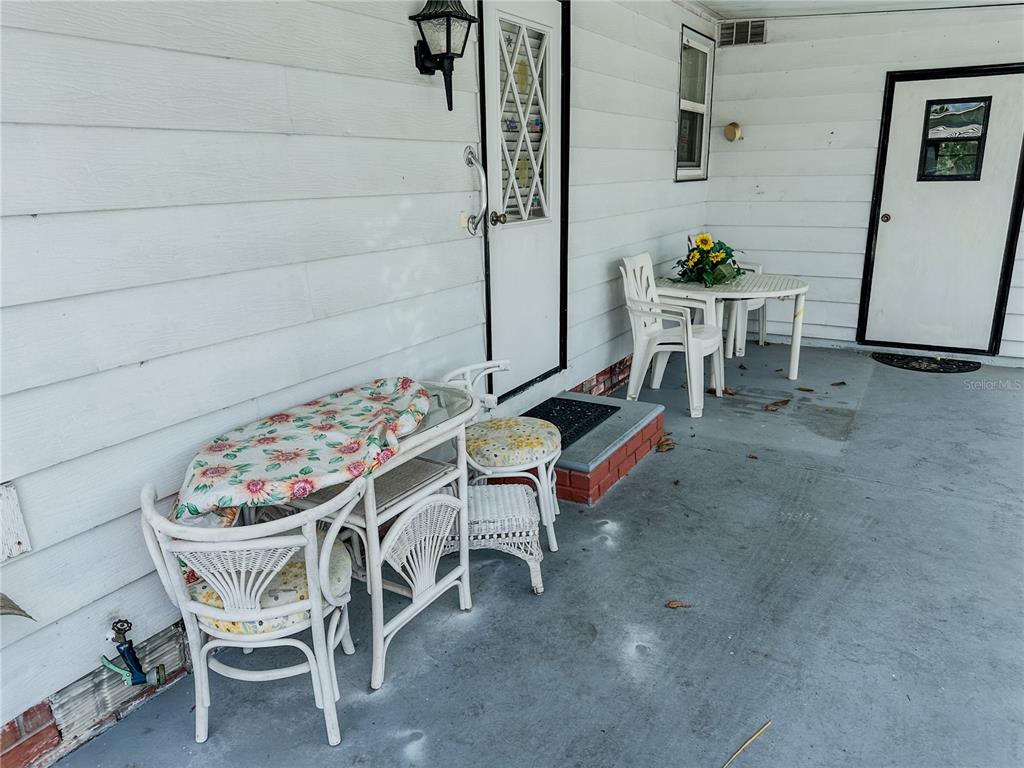 A covered patio features white siding, two sets of patio furniture, and two exterior doors — 1820 W SCHWARTZ BOULEVARD, LADY LAKE, FL