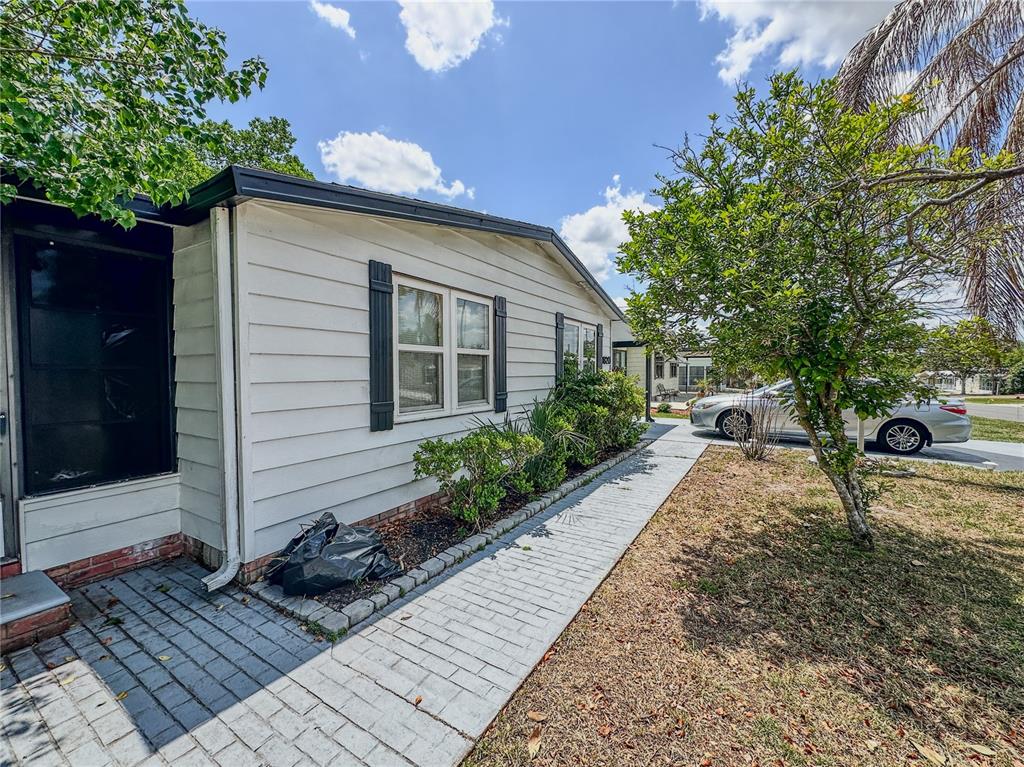 A white mobile home exterior features a paved walkway, landscaping, and a parked silver car — 1820 W SCHWARTZ BOULEVARD, LADY LAKE, FL