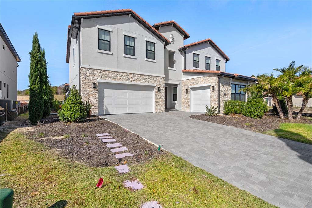 A two-story house features a stone facade, a paved driveway, and a three-car garage — 16829 BOLSENA DRIVE, MONTVERDE, FL