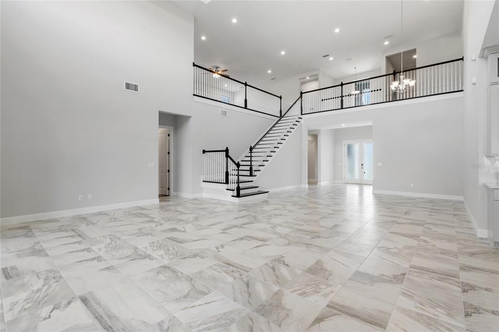 A spacious, high-ceilinged foyer features white walls, marble-look tile flooring, and a black-railed staircase — 16829 BOLSENA DRIVE, MONTVERDE, FL