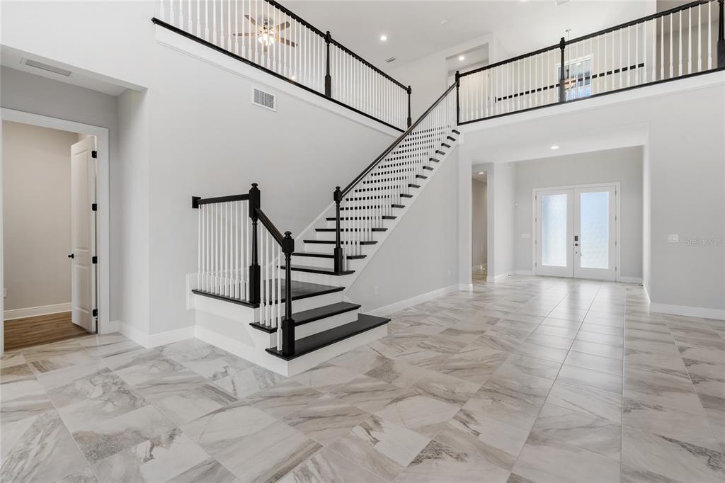 A bright foyer features a grand staircase with black railings and light marble-patterned tile flooring — 16829 BOLSENA DRIVE, MONTVERDE, FL