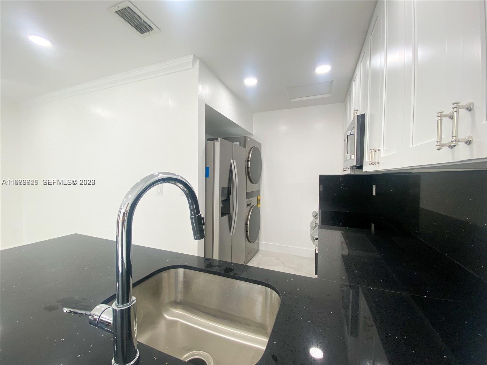 A kitchen features black countertops, white cabinets, a stainless steel sink, and a stacked laundry unit — 2550 W 67th Pl # 32, Hialeah FL 33016, HIALEAH, FL