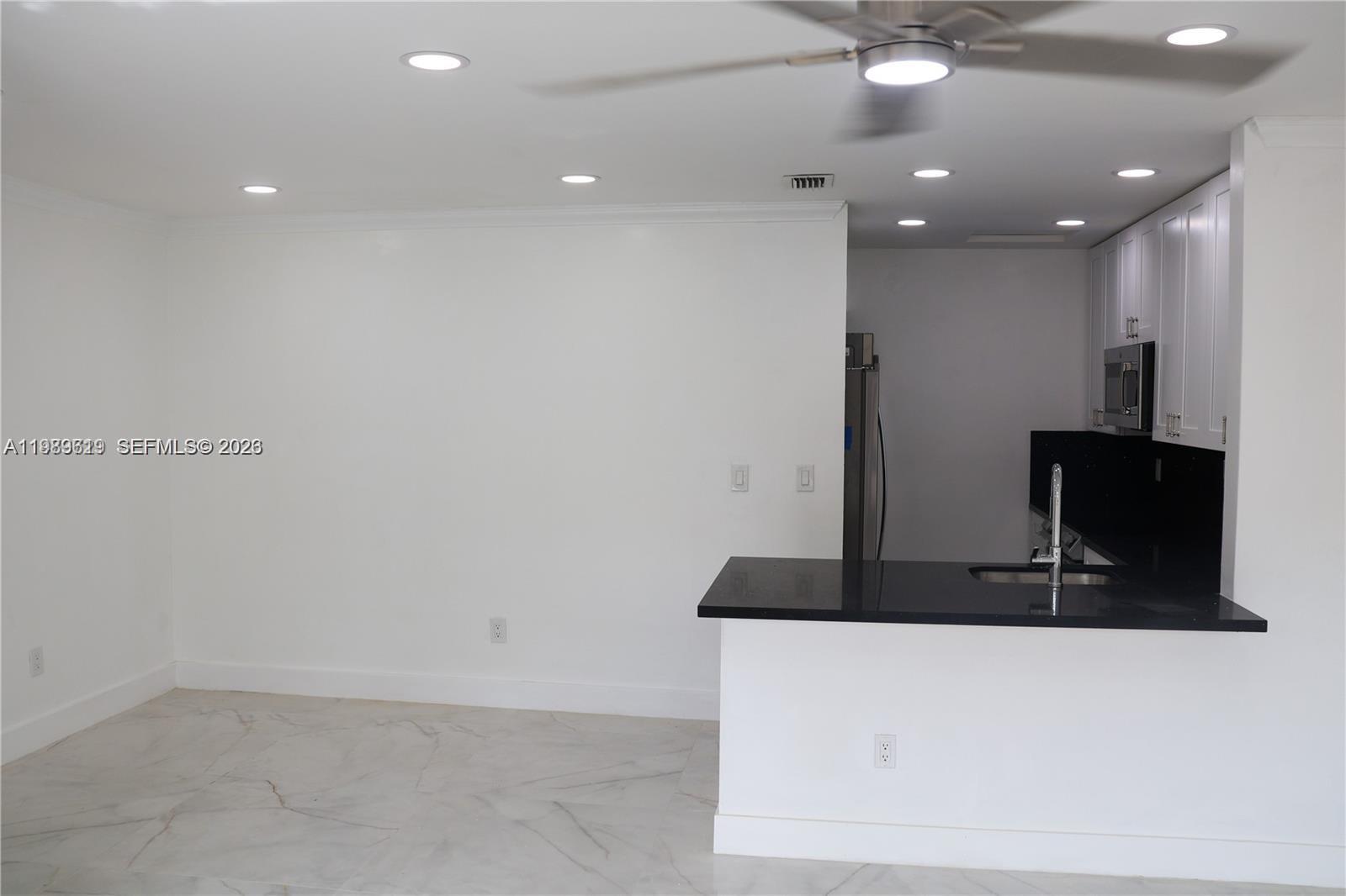 A kitchen with a black countertop island and white cabinets opens to a dining area — 2550 W 67th Pl # 32, Hialeah FL 33016, HIALEAH, FL