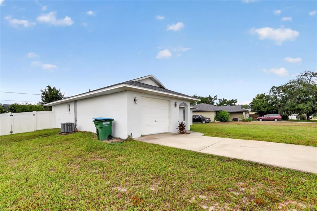 A white single-story house exterior features a garage, a concrete driveway, and a green trash bin — 2941 BEDFORD STREET, DELTONA, FL