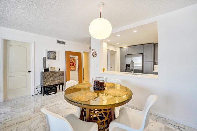A dining area with a glass-topped table, white chairs, and a view into the kitchen — 401 NE 14th Avenue # 705, FL 33009, FL