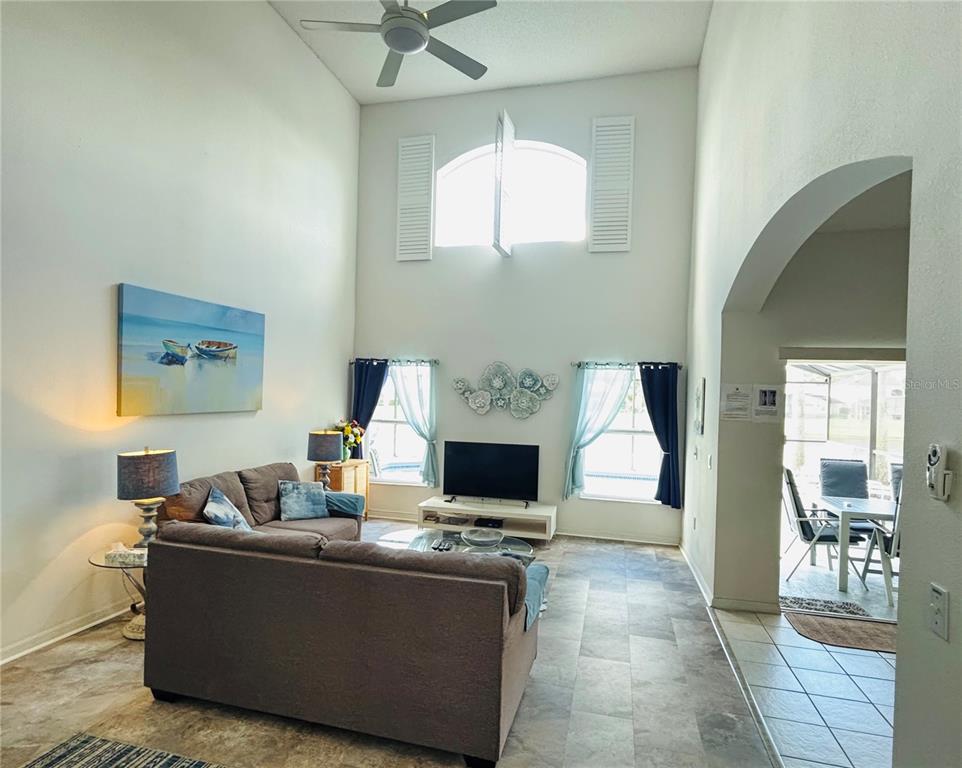 A living room with high ceilings, tile floors, a sofa, and a television — 936 LAKE BERKLEY DRIVE, KISSIMMEE, FL