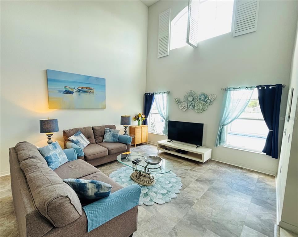 A living room with high ceilings, tile floors, two brown sofas, and a glass coffee table — 936 LAKE BERKLEY DRIVE, KISSIMMEE, FL