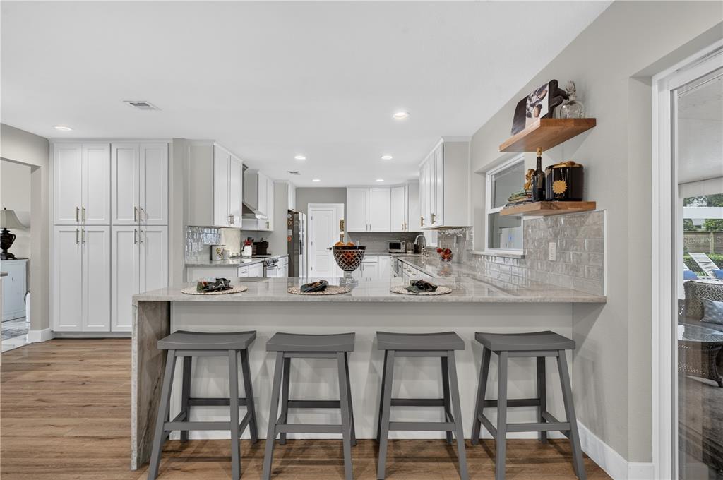 A modern kitchen features white cabinets, a stone waterfall island with four stools, and wood flooring — 165 LAKE DESTINY TRAIL, ALTAMONTE SPRINGS, FL