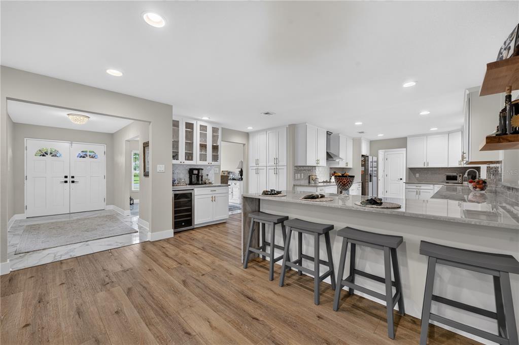 A modern kitchen features white cabinetry, a large granite island with bar stools, and wood flooring — 165 LAKE DESTINY TRAIL, ALTAMONTE SPRINGS, FL