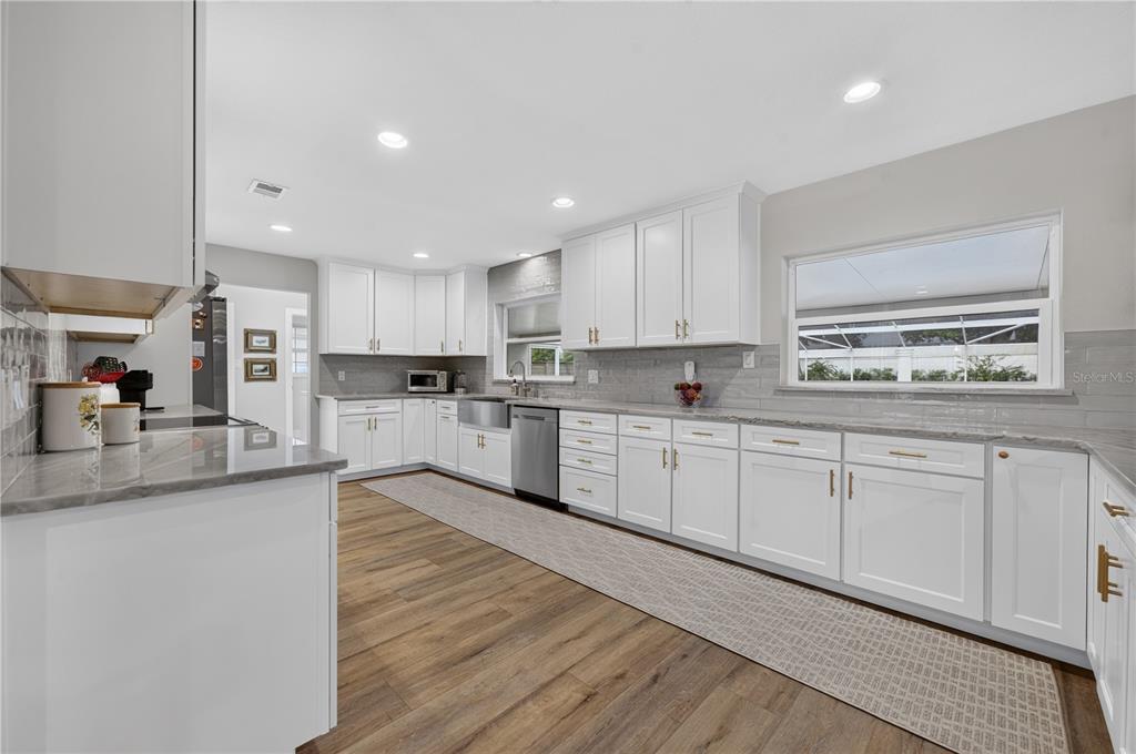 A bright kitchen features white cabinets, gray countertops, a farmhouse sink, and wood-look flooring — 165 LAKE DESTINY TRAIL, ALTAMONTE SPRINGS, FL