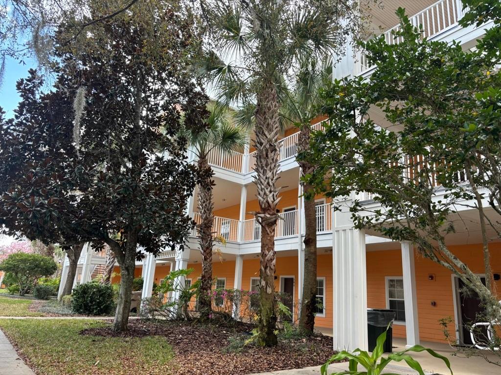 A three-story orange apartment building with white balconies and palm trees in the foreground — 115 ROGUES RETREAT UNIT 115, DAVENPORT, FL