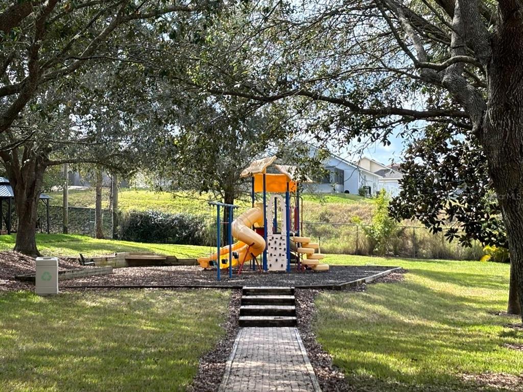 A playground with a yellow slide and climbing wall sits in a grassy park area — 115 ROGUES RETREAT UNIT 115, DAVENPORT, FL