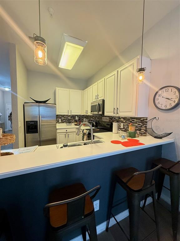 A kitchen features white cabinets, stainless steel appliances, a breakfast bar, and two pendant lights — 115 ROGUES RETREAT UNIT 115, DAVENPORT, FL